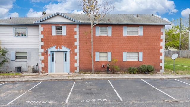 view of property with uncovered parking, central AC unit, and fence