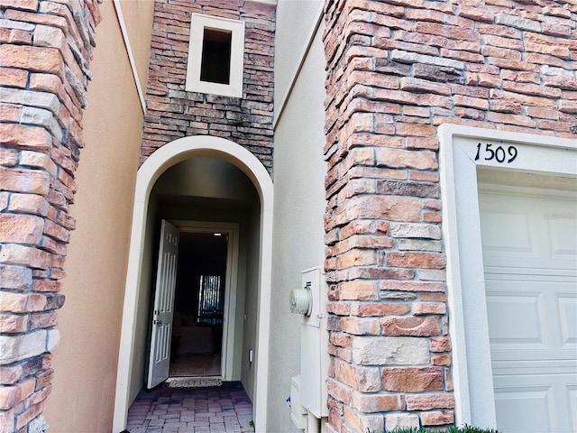 view of exterior entry featuring a garage and brick siding