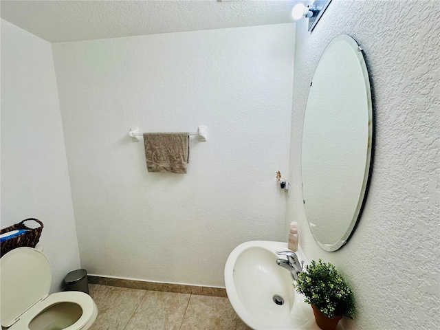 bathroom with baseboards, toilet, tile patterned floors, a textured ceiling, and a sink