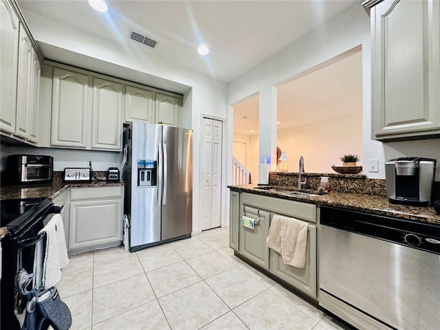 kitchen featuring stainless steel appliances, visible vents, light tile patterned flooring, a sink, and dark stone countertops