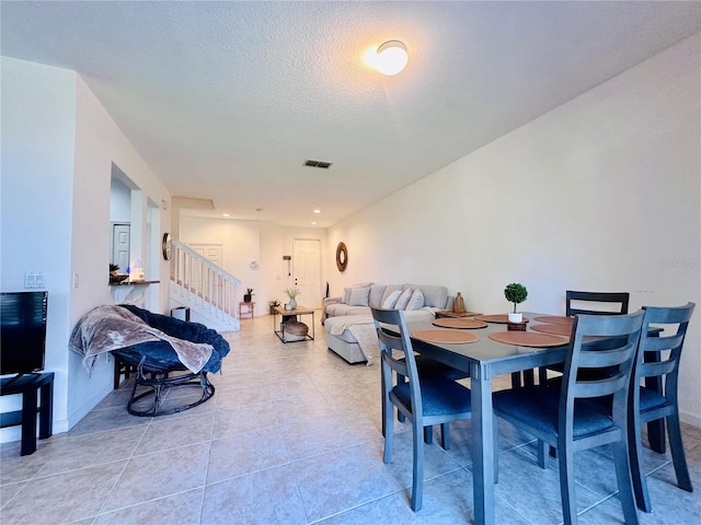 dining space with light tile patterned floors, stairs, visible vents, and a textured ceiling