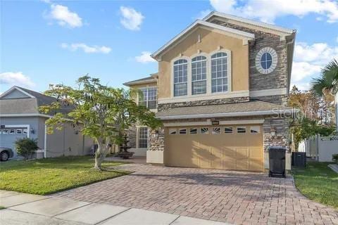 traditional home with a garage, a front lawn, decorative driveway, and stucco siding