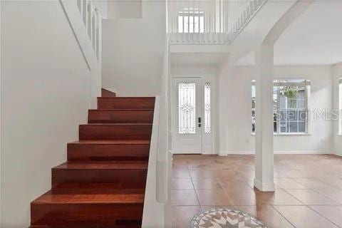 tiled entrance foyer with a towering ceiling, stairs, and arched walkways