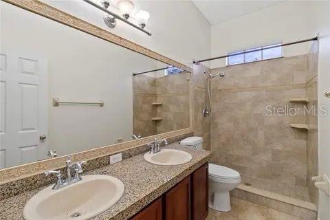 full bath with double vanity, tiled shower, a sink, and toilet