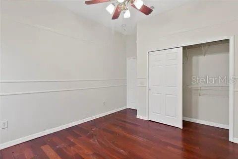 unfurnished bedroom featuring ceiling fan, dark wood-style flooring, a closet, and baseboards