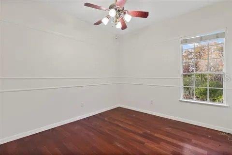 empty room featuring ceiling fan, baseboards, and dark wood-type flooring