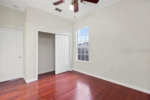 unfurnished bedroom featuring dark wood-style flooring, a ceiling fan, visible vents, baseboards, and a closet