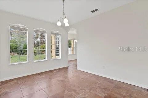 spare room featuring lofted ceiling, baseboards, visible vents, and a notable chandelier