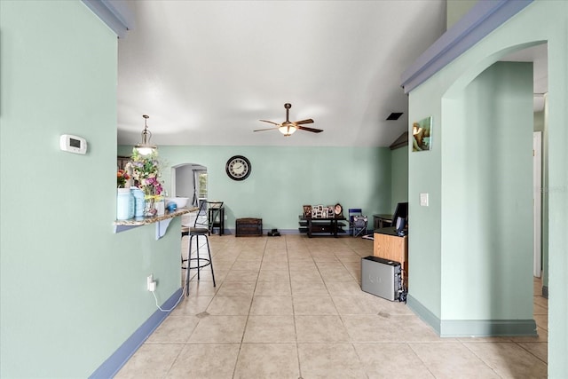 interior space featuring arched walkways, light tile patterned floors, a breakfast bar area, a ceiling fan, and baseboards