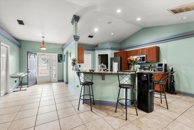 kitchen featuring appliances with stainless steel finishes, brown cabinetry, visible vents, and a kitchen bar