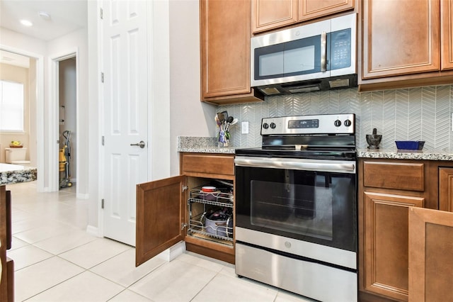 kitchen with light tile patterned floors, stainless steel appliances, light stone counters, and decorative backsplash