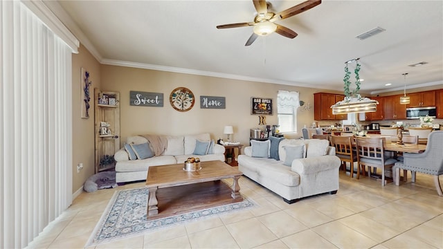 living area with light tile patterned floors, visible vents, baseboards, a ceiling fan, and crown molding