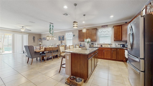 kitchen featuring visible vents, a kitchen island, decorative light fixtures, freestanding refrigerator, and light stone countertops