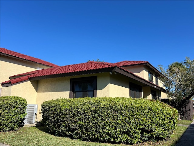 view of property exterior featuring central AC, a tiled roof, and stucco siding