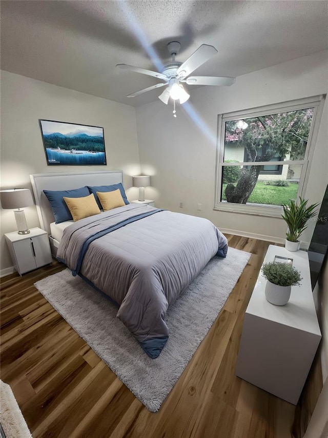 bedroom with a textured ceiling, wood finished floors, a ceiling fan, and baseboards