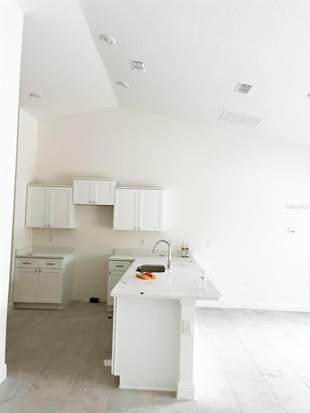 kitchen featuring a peninsula, a sink, white cabinets, vaulted ceiling, and light countertops