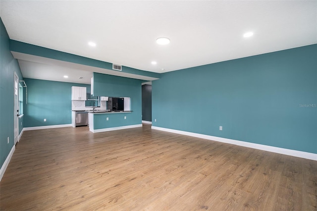 unfurnished living room with dark wood-type flooring, recessed lighting, a sink, and baseboards