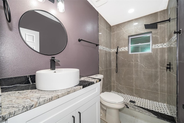 bathroom with toilet, a textured wall, a tile shower, and vanity