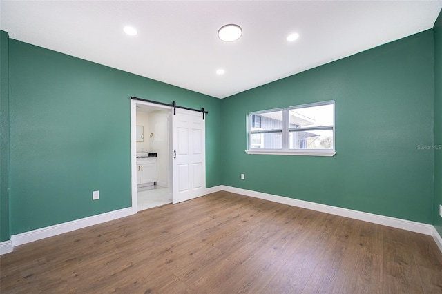 unfurnished bedroom featuring recessed lighting, wood finished floors, baseboards, and a barn door