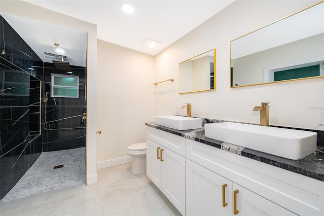 bathroom featuring marble finish floor, tiled shower, a sink, and toilet