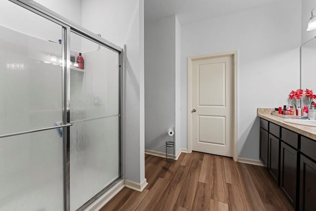 full bathroom with a stall shower, vanity, baseboards, and wood finished floors