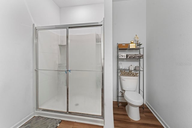 bathroom featuring toilet, a shower stall, baseboards, and wood finished floors