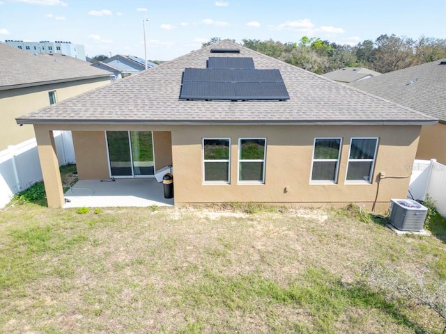 rear view of house with central air condition unit, a lawn, a patio, and roof with shingles