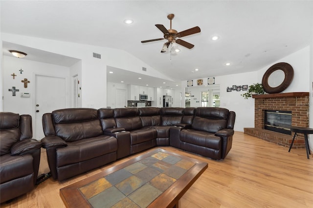 living area with light wood finished floors, visible vents, a brick fireplace, vaulted ceiling, and ceiling fan