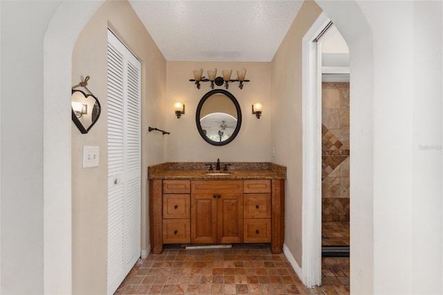 full bath featuring a closet, a tile shower, vanity, and baseboards