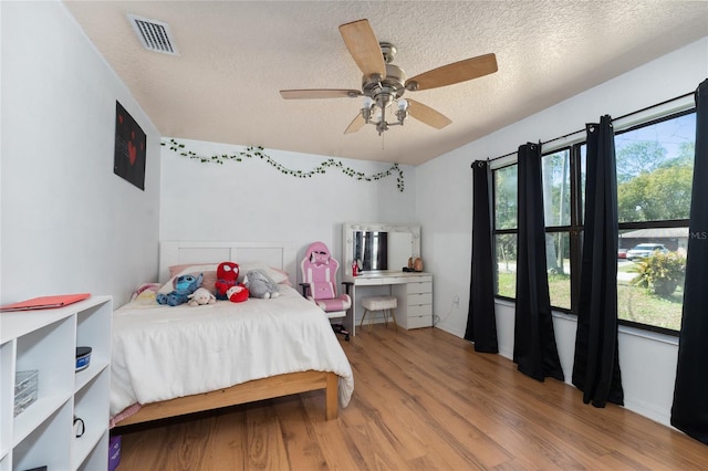 bedroom with a textured ceiling, visible vents, wood finished floors, and multiple windows