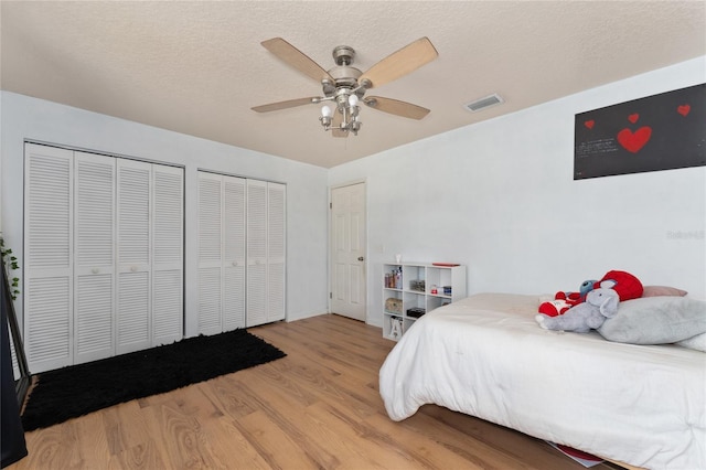 bedroom featuring multiple closets, visible vents, ceiling fan, a textured ceiling, and wood finished floors