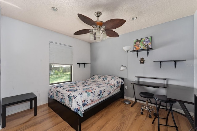 bedroom featuring a ceiling fan, a textured ceiling, baseboards, and wood finished floors