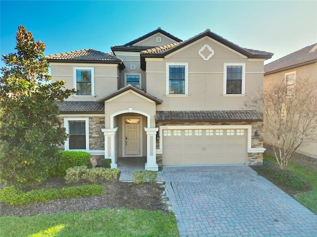 view of front of property featuring decorative driveway, stone siding, a tiled roof, and stucco siding