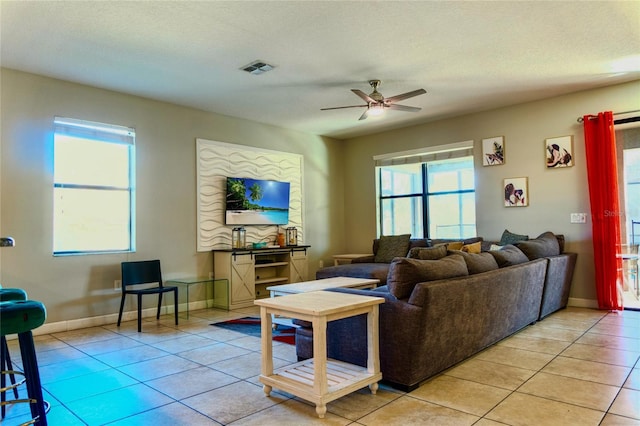 living room featuring light tile patterned floors, a textured ceiling, visible vents, a ceiling fan, and baseboards