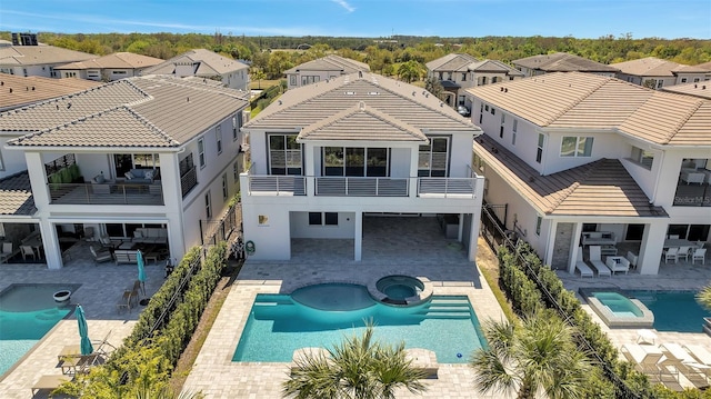 rear view of house with a pool with connected hot tub, a residential view, stucco siding, a balcony, and a patio