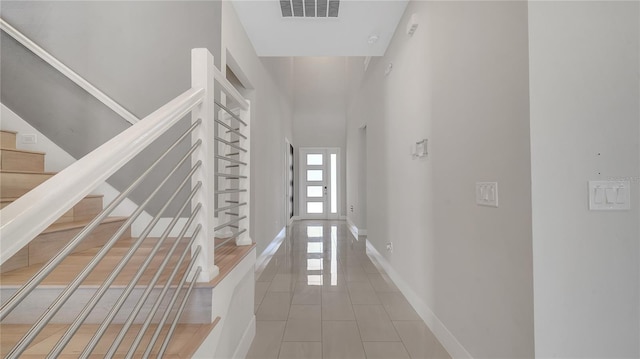 hallway featuring stairway, baseboards, visible vents, a towering ceiling, and tile patterned floors