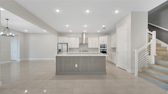 kitchen featuring an inviting chandelier, light countertops, appliances with stainless steel finishes, white cabinetry, and wall chimney range hood