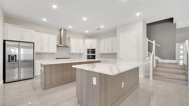 kitchen with a spacious island, wall chimney range hood, decorative backsplash, stainless steel appliances, and white cabinetry