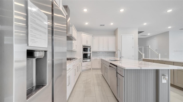 kitchen featuring visible vents, a sink, stainless steel appliances, wall chimney range hood, and decorative backsplash