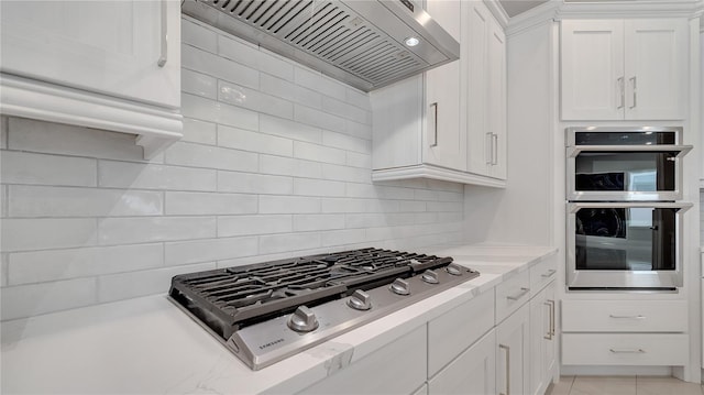 kitchen with tasteful backsplash, wall chimney range hood, light stone counters, appliances with stainless steel finishes, and white cabinets