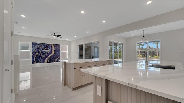 kitchen featuring a kitchen island with sink, ceiling fan with notable chandelier, a sink, recessed lighting, and light stone countertops