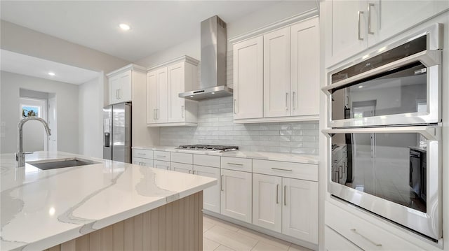 kitchen featuring light tile patterned flooring, a sink, stainless steel appliances, wall chimney range hood, and tasteful backsplash