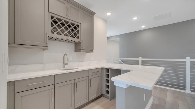 kitchen with a sink, a peninsula, light stone countertops, and gray cabinetry