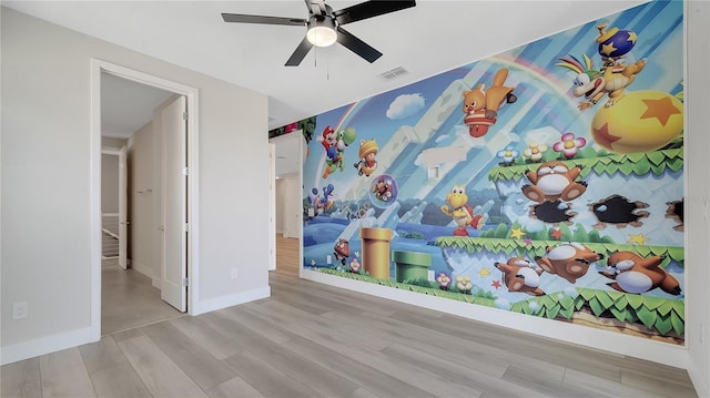 unfurnished bedroom with visible vents, an accent wall, baseboards, wood finished floors, and a ceiling fan