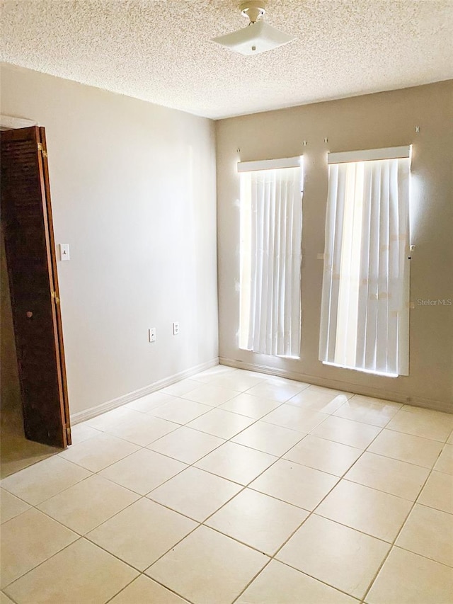 spare room featuring a textured ceiling, baseboards, and light tile patterned floors