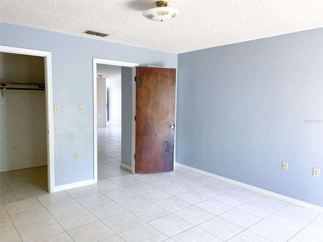 unfurnished bedroom featuring light tile patterned floors, a closet, visible vents, a textured ceiling, and baseboards