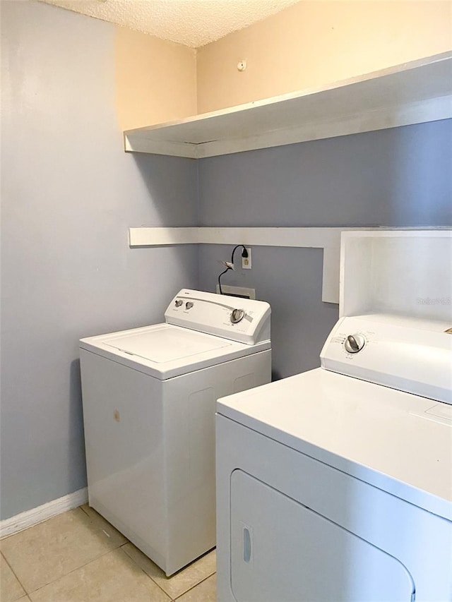 laundry area featuring laundry area, light tile patterned floors, baseboards, a textured ceiling, and washing machine and dryer