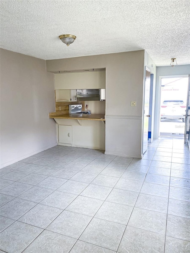 kitchen featuring a textured ceiling, light tile patterned flooring, under cabinet range hood, a kitchen breakfast bar, and baseboards