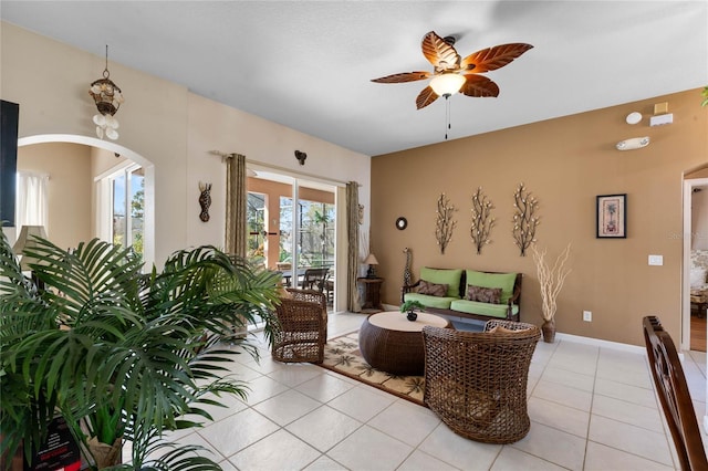 living area featuring a ceiling fan, arched walkways, baseboards, and light tile patterned floors