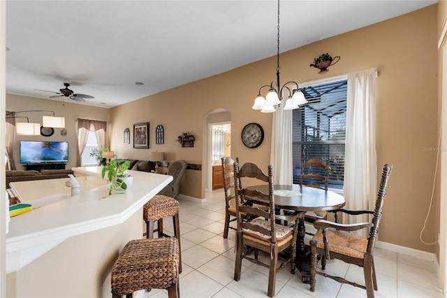 dining area featuring arched walkways, ceiling fan, light tile patterned flooring, and baseboards